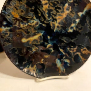 May include: A black ceramic plate with a swirling pattern of blue, brown, and gold.