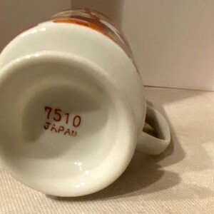 May include: White ceramic mug with a brown and orange floral design. The bottom of the mug has the text "7510 JAPAN" printed in red.