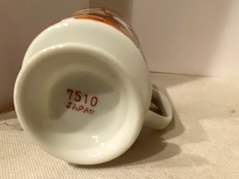 May include: White ceramic mug with a brown and orange floral design. The bottom of the mug has the text "7510 JAPAN" printed in red.