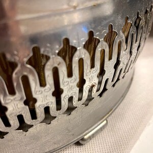 May include: Silver metal bowl with a decorative, ornate design. The bowl has a scalloped edge and a raised, intricate pattern.