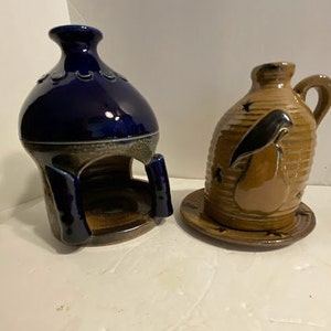 May include: Two ceramic candle holders, one blue and one brown with a bird design. The blue holder has a round opening in the top and the brown holder has a small plate underneath.
