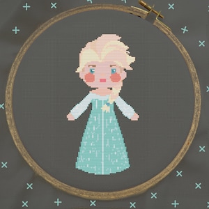 Può includere: Ricamo a punto croce di un personaggio dei cartoni animati che indossa un vestito blu e bianco con un motivo a fiocco di neve. Il personaggio ha i capelli biondi e un viso rosa chiaro.