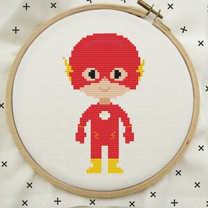 May include: Cross-stitch embroidery hoop with a red and yellow cartoon character of The Flash, a superhero with lightning bolts on his suit.