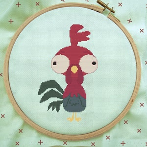 May include: A cross-stitch embroidery hoop with a red rooster with large eyes and a black tail. The rooster is on a light green background.