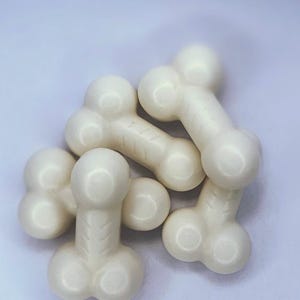 Può includere: Un gruppo di caramelle bianche a forma di fallo. Le caramelle hanno una finitura liscia e lucida e sono disposte su uno sfondo chiaro. Le forme sono dettagliate con teste e basi arrotondate.