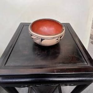 May include: A small, round, terracotta bowl with a white geometric design. The bowl has a red interior and is decorated with black and white lines.