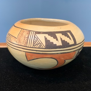 May include: A small, round, cream-colored pottery bowl with black and orange geometric designs.