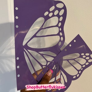 May include: Purple butterfly stencil with a cut-out design. The stencil is held in a hand with a pink and white nail design. The text "ShopButterflykisses" is visible in the image.