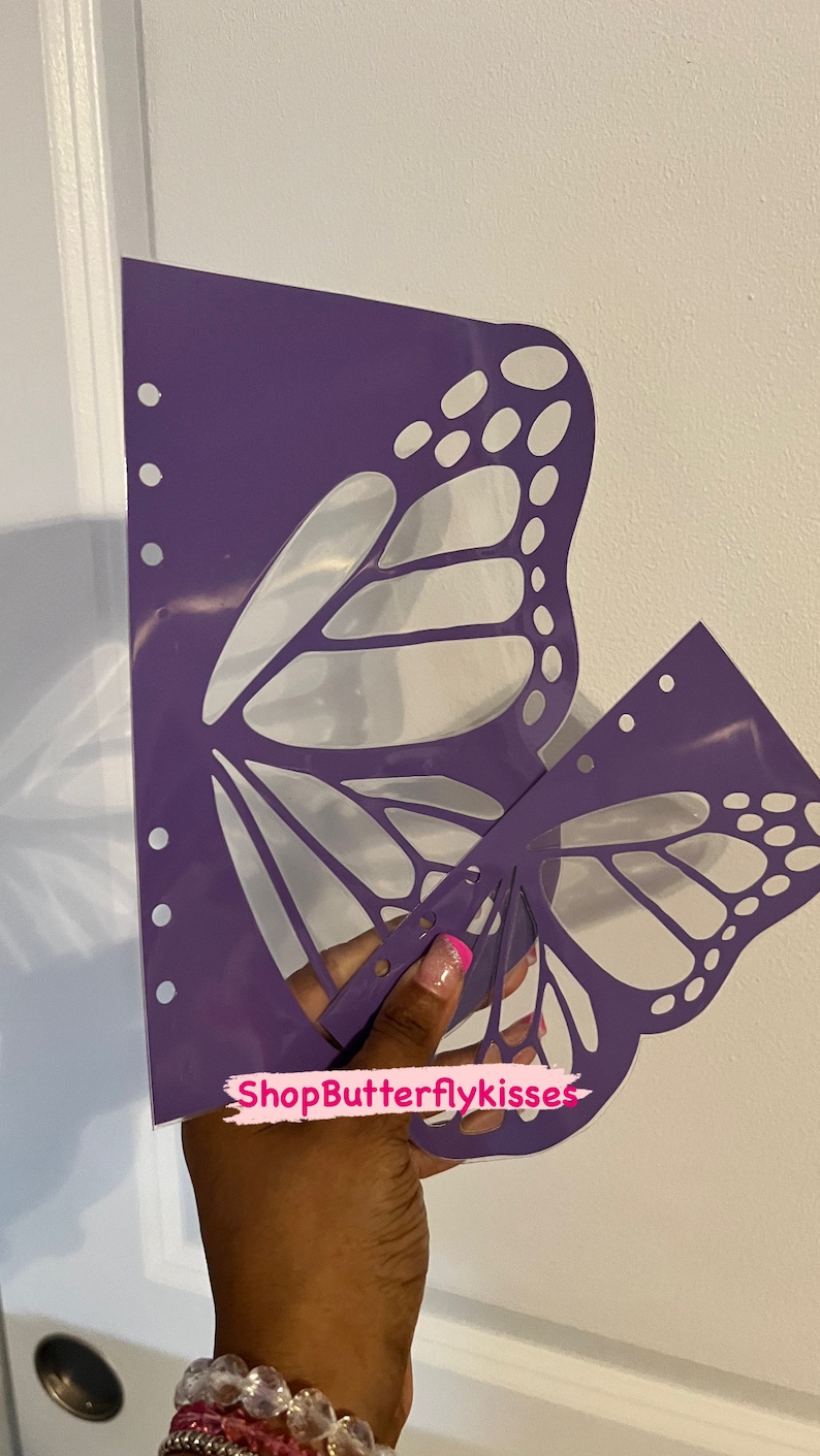 May include: Purple butterfly stencil with a cut-out design. The stencil is held in a hand with a pink and white nail design. The text "ShopButterflykisses" is visible in the image.