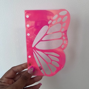 May include: A pink butterfly-shaped plastic planner page with holes on the left side. The butterfly design is cut out, revealing a white background.
