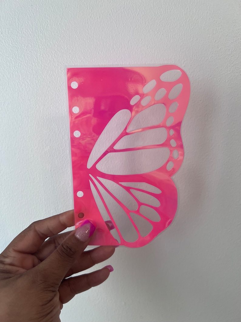 May include: A pink butterfly-shaped plastic planner page with holes on the left side. The butterfly design is cut out, revealing a white background.