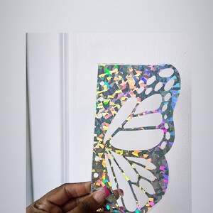 May include: A holographic butterfly wing stencil with a white butterfly design. The stencil is made of a clear, iridescent material.
