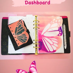 May include: A pink and white butterfly-shaped laminated dashboard insert for a planner or notebook. The insert is designed to be used as a decorative element and to help organize pages. The insert is shown in a planner with a gold ring binder.