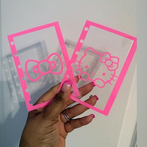 Peut inclure: Deux intercalaires de planificateur roses et transparents sur le thème Hello Kitty. L'un présente un motif de nœud, l'autre le personnage Hello Kitty. Les intercalaires ont une bordure rose.