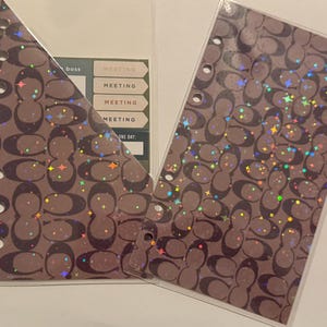 Peut inclure: Deux inserts de planificateur avec un motif marron et des paillettes holographiques. Un insert a une poche triangulaire avec des étiquettes de réunion. L'autre insert est rectangulaire avec plusieurs trous pour la reliure.