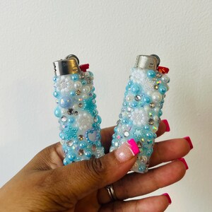 Pu&ograve; includere: Due accendini blu e bianchi decorati con perle e strass. Gli accendini hanno una parte superiore argentata e un pulsante rosso.