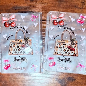 May include: Four clear plastic organizers with a Coach design. Each features a leopard print handbag, cherries, bows, hearts, and a horse-drawn carriage. The Coach logo is visible. The organizers are arranged on a wooden surface.