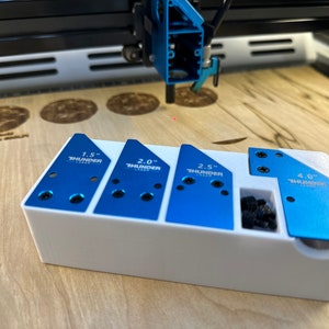 May include: A white plastic organizer with four blue metal jigs for woodworking. The jigs are labeled "1.5", "2.0", "2.5", and "4.0" with the word "THUNDER" printed on each. The jigs are designed for use with a laser cutter.