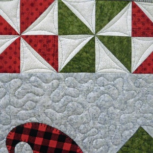 May include: A close-up of a quilt with a red, white, and green patchwork design. The quilt is quilted with a swirling pattern. The quilt is made of cotton fabric.