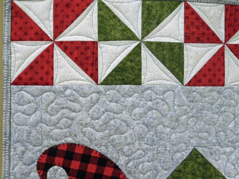 May include: A close-up of a quilt with a red, white, and green patchwork design. The quilt is quilted with a swirling pattern. The quilt is made of cotton fabric.