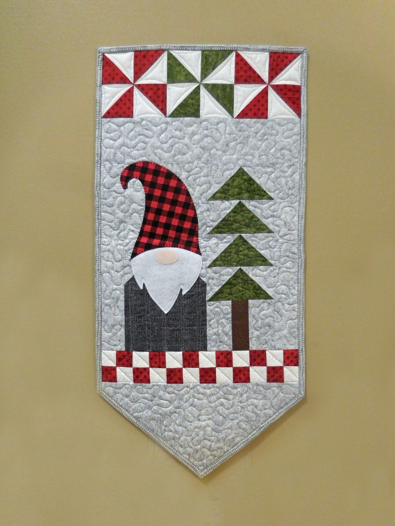 May include: A gray quilted fabric banner with a red and black plaid gnome, a green tree, and a red and white checkered border.