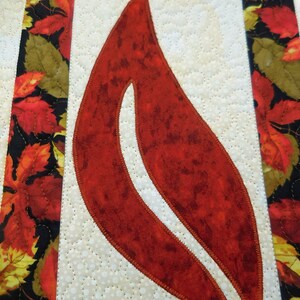 以下が含まれることがあります： 白い背景に赤い布の葉。葉は茶色の糸で縫われており、まだら模様の質感がある。