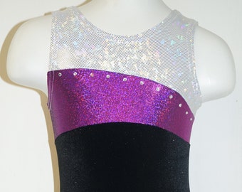 May include: A black, purple, and white leotard with rhinestones. The leotard has a mesh top, a purple glitter bodice, and a black velvet skirt.