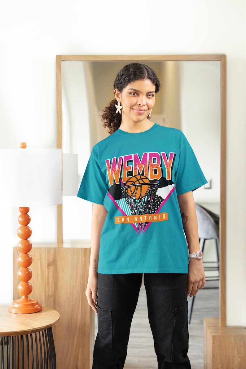 May include: A turquoise t-shirt with a graphic print of a basketball player dunking a basketball. The graphic includes the text "WEMBY" and "SAN ANTONIO".