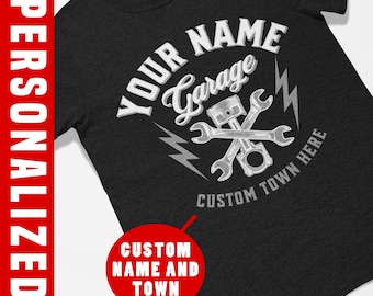 May include: Black t-shirt with a white graphic design of crossed wrenches, a piston, and lightning bolts. The text "Your Name Garage" is in a circle above the wrenches. The text "Custom Town Here" is below the wrenches.