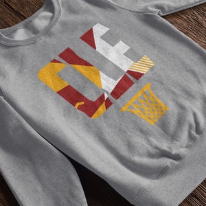 May include: Gray sweatshirt with a graphic of the letters "CLE" in red, yellow, and white, with a basketball hoop and net in yellow.