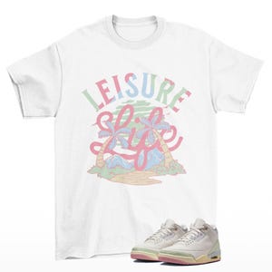 May include: White t-shirt with the words "LEISURE LIFE" in pastel colors and a tropical graphic. Below the shirt are white and light green sneakers with pink and yellow accents.