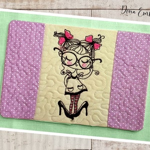 May include: Embroidered design of a girl with glasses and pigtails wearing a dress and high heels. The design is on a light yellow fabric with a purple and white polka dot border.