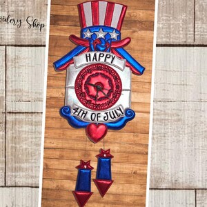 Pode incluir: Decoração patriótica do 4 de julho com um design de chapéu do Tio Sam vermelho, branco e azul. A decoração inclui o texto "HAPPY 4TH OF JULY" e um mostrador de relógio. Dois ornamentos em forma de estrela penduram-se por baixo.