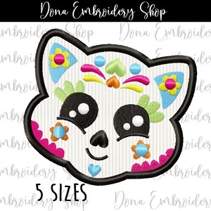May include: Embroidered design of a white sugar skull with black eyes, a pink and blue flower on each side, and a pink, yellow, and green floral design on the top. The skull has a smiling mouth and a small blue heart on the chin. The design is available in 5 sizes.