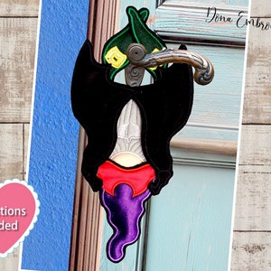 May include: A purple and red Halloween door hanger with a black bat and a green hat. The door hanger is attached to a door handle. The text "Dona Embroidery Shop" is visible in the background.
