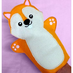 May include: A felt hand puppet shaped like a squirrel with orange fur, white belly, and pink ears. The puppet has a black nose, white teeth, and black eyes.