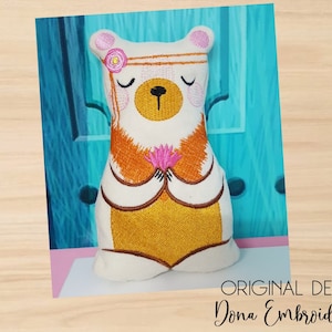May include: White plush bear with a pink flower headband, brown eyes, and a pink flower in its paws. The bear is wearing a yellow and orange outfit and is sitting in a meditative pose.  Original Design by: Dona Embroidery Shop