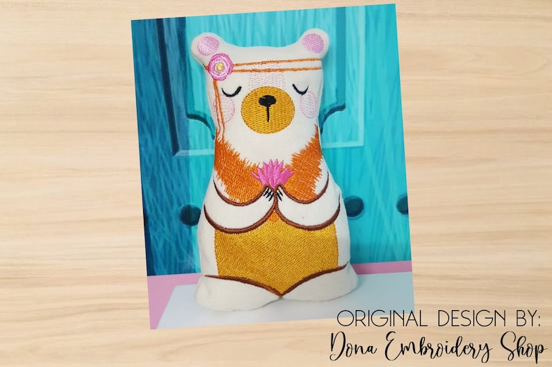 May include: White plush bear with a pink flower headband, brown eyes, and a pink flower in its paws. The bear is wearing a yellow and orange outfit and is sitting in a meditative pose.  Original Design by: Dona Embroidery Shop