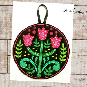 May include: A round, black felt ornament with a pink, green, and yellow embroidered floral design. The ornament has a black ribbon loop for hanging.