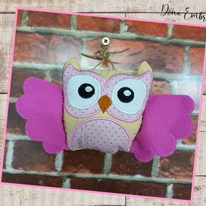 May include: A plush owl toy with pink wings and a beige body with pink polka dots. The owl has large black eyes with white pupils and a small orange beak.