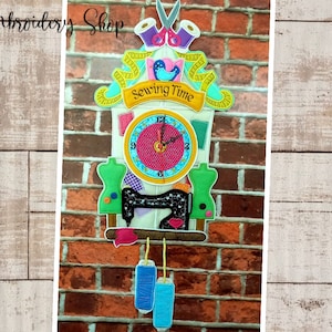 Pode incluir: Um relógio de cuco colorido com tema de costura. O mostrador do relógio tem um fundo rosa com números e ponteiros pretos. O relógio é decorado com itens relacionados à costura, como tesouras, carretéis de linha e uma máquina de costura. O relógio está pendurado em uma parede de tijolos. O texto "Sewing Time" está no relógio.