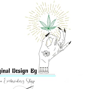 Pode incluir: Um desenho de linha preta de uma mão com um olho e um design de lua crescente segurando uma folha de maconha verde com um brilho de sol dourado atrás. O texto "Original Design By" e "Dina Embroidery Shop" está abaixo da imagem.