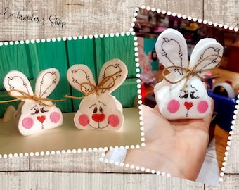 May include: Three white felt bunny-shaped Easter baskets with embroidered faces. The baskets are tied with twine and have pink cheeks and red noses.
