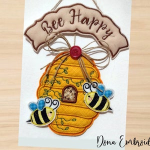 Pode incluir: Uma colmeia amarela e marrom com duas abelhas de cada lado. A colmeia tem uma pequena janela e videiras crescendo pelo lado. Uma faixa acima da colmeia diz "Bee Happy".