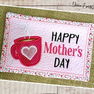 May include: A pink and white quilted coaster with a red coffee cup and the text "HAPPY Mother's DAY" embroidered on it.