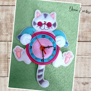 May include: A white cat with gray stripes holding a pink and blue clock with gold stars. The clock has black hands and a white face with black numbers. The cat's tail is also gray and striped.