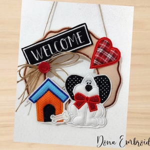 Pode incluir: Uma coroa de boas-vindas com um cão preto e branco, um coração vermelho, uma casinha de cachorro e uma placa de boas-vindas. A coroa é feita de juta e tem um fundo marrom.