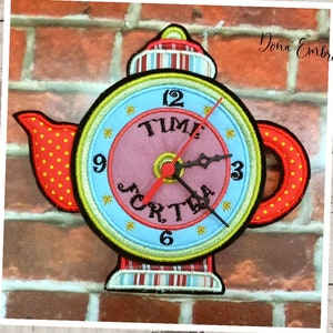 Pode incluir: Um relógio de chá bordado colorido com detalhes vermelhos, amarelos, azuis e verdes. O mostrador do relógio diz "Time for Tea" e tem um ponteiro das horas preto e um ponteiro dos minutos vermelho.