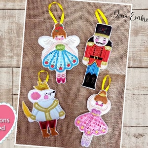 Peut inclure: Quatre ornements en feutre brodés représentant des personnages du ballet Casse-Noisette. Les ornements sont une ballerine en robe bleue, un casse-noisette soldat en rouge et bleu, une souris avec une couronne dorée et une ballerine en robe rose.