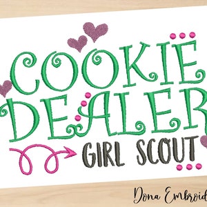 Könnte beinhalten: Stickerei mit dem Text "Cookie Dealer: Girl Scout" in Grün, Pink und Grau. Das Design enthält Herzen und Schnörkel.